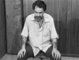 a black and white photo of a man with a beard kneeling down in a chair .