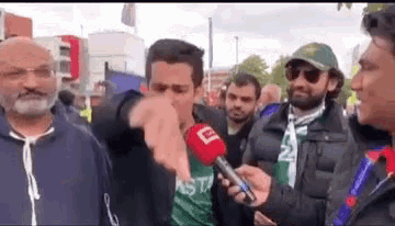 a man is pointing at another man while holding a microphone in front of a crowd of people .