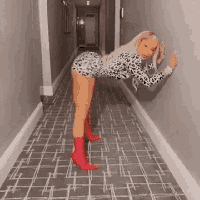 a woman is leaning against a wall in a hallway while wearing a leopard print dress and red boots .