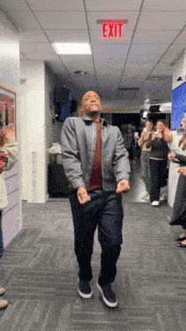 a man in a grey jacket is dancing in front of an exit sign
