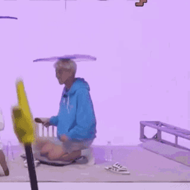 a man in a blue hoodie is kneeling down in front of a purple wall while holding a yellow object .
