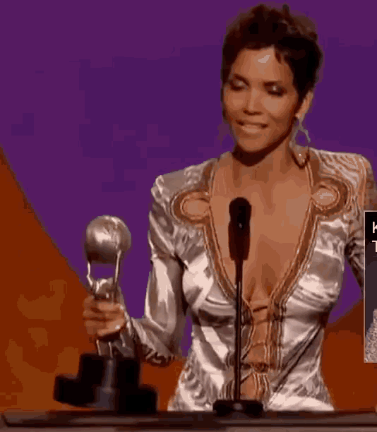a woman with a very plunging neckline is holding a trophy and speaking into a microphone