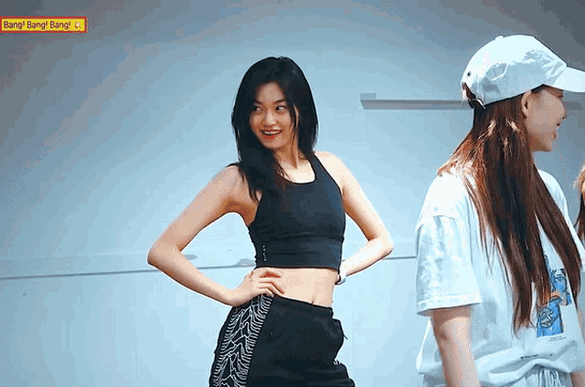 a woman in a black crop top stands next to another woman in a white hat with bang bang bang written on the bottom