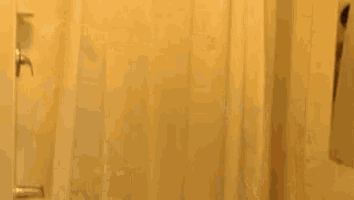 a man in a suit is pulling up a shower curtain in a bathroom with the word surprise written on it .