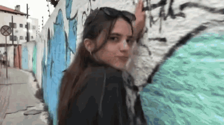a woman is standing in front of a wall with graffiti on it