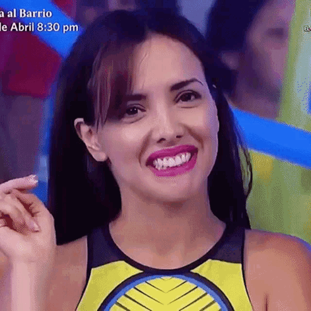 a woman in a yellow and black tank top is smiling and making a funny face .