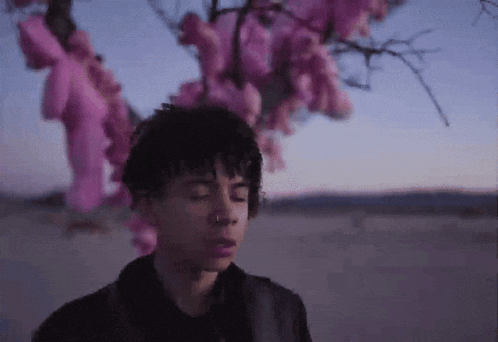 a young man standing in front of a tree with pink flowers