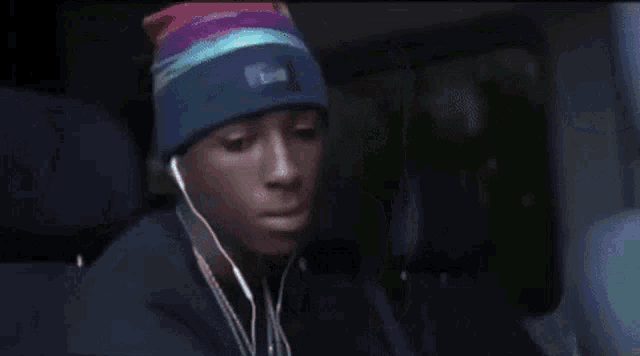 a man wearing a rainbow hat and earbuds is giving the middle finger .