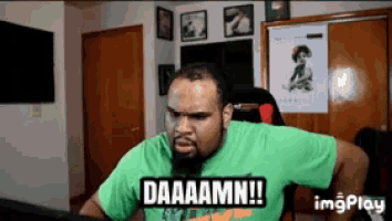 a man in a green shirt says " daaaamm " in front of a computer screen