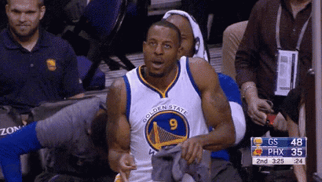 a man in a golden state warriors jersey is sitting in the stands during a basketball game .