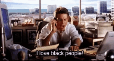 a man sitting at a desk talking on a cell phone with the words i love black people below him