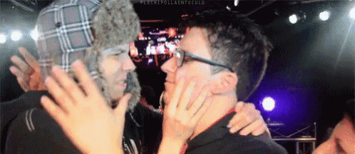a man wearing a fur hat and glasses is kissing another man 's face .