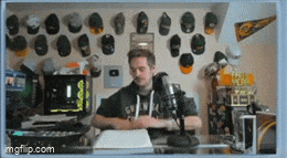 a man is sitting in front of a microphone in a room with baseball caps hanging on the wall
