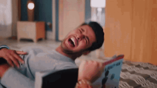 a man is laying on a bed with his mouth open while a woman holds his chest .
