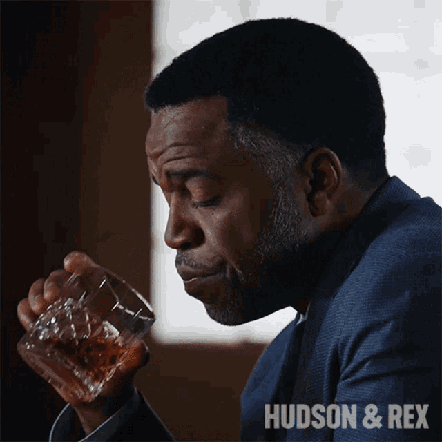 a man drinking a glass of whiskey with the words hudson & rex above him