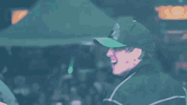 a man wearing a green hat is laughing in front of a crowd of people .