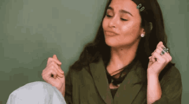 a woman in a green jacket is making a heart shape with her hands