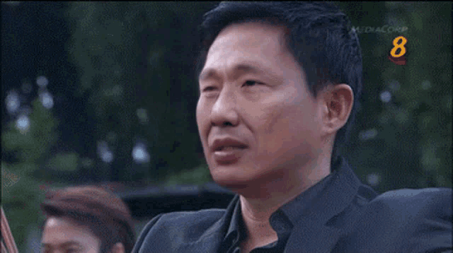 a man wearing a watch holds his hand to his forehead in front of a sign that says mediacorp 8