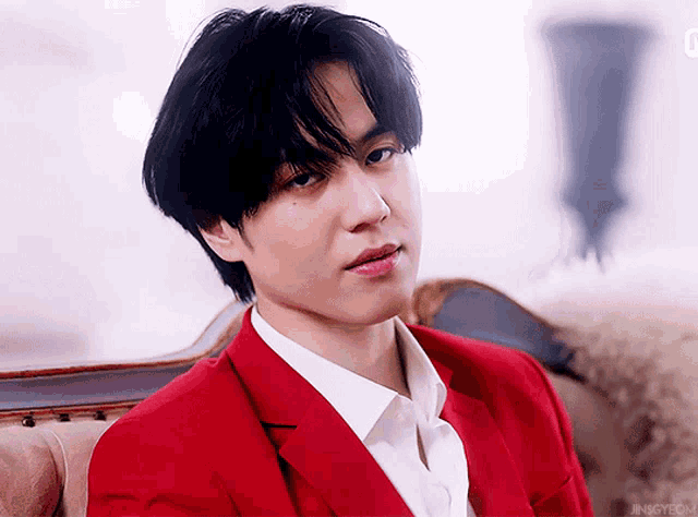 a young man wearing a red suit and white shirt is sitting on a couch