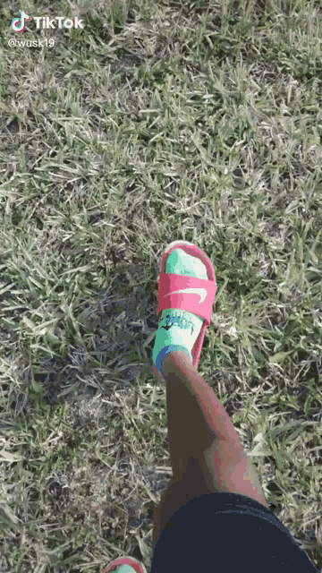 a person wearing a pair of nike slides and a pair of socks is standing in the grass .