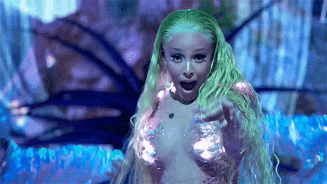 a woman with green hair is wearing a mermaid costume and making a funny face .