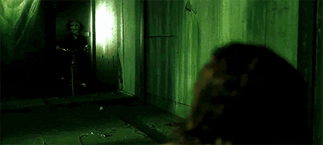 a person is standing in a dark room looking at a person on a bike with a mask on .