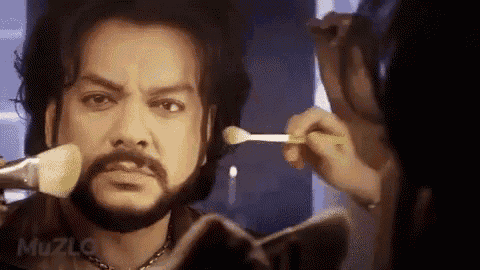 a man with a beard is getting his makeup applied by a woman .