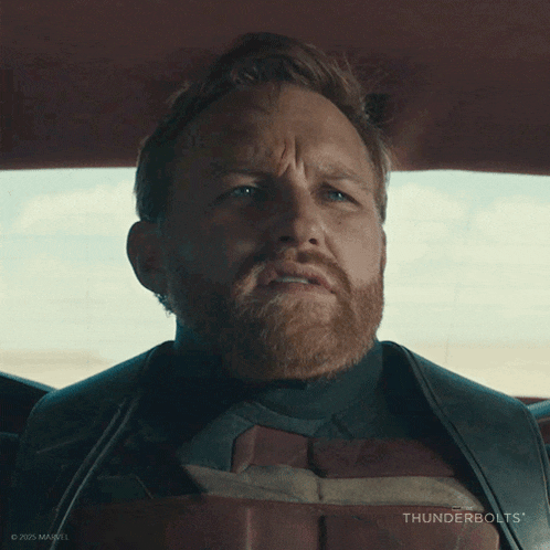 a man with a beard is sitting in a car with thunderbolts written on the bottom of the image