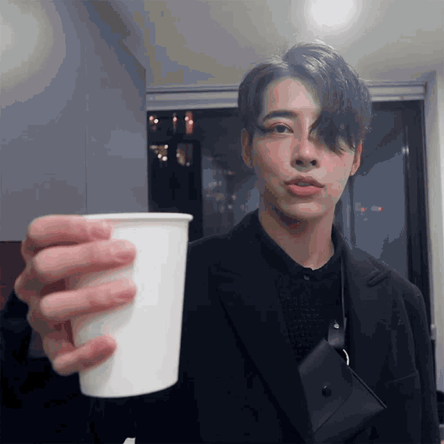 a man in a black suit holds a white cup in his hand