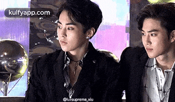 two men in suits are sitting next to each other and looking at each other .