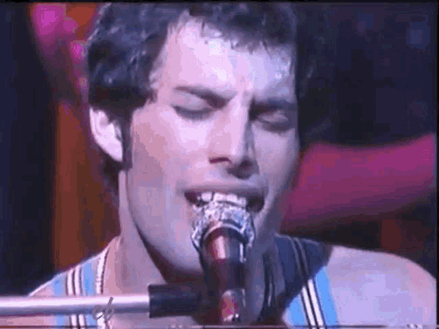 a man is singing into a microphone with his eyes closed .