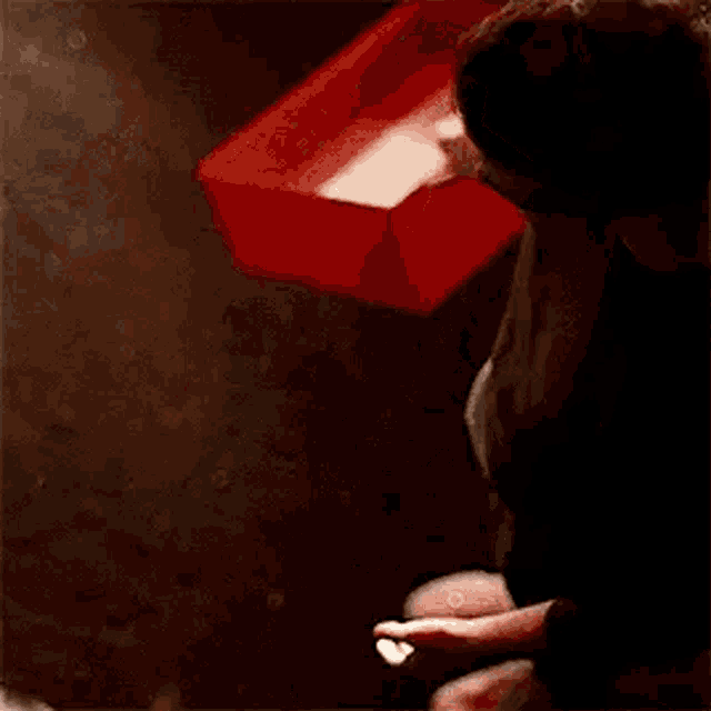a woman is sitting on the floor in a dark room holding a red object in her hands .
