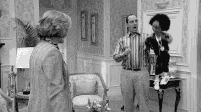 a man and a woman are standing in a living room talking to each other in a black and white photo .