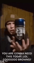 a man in a hat is holding a can of beer in his hands .