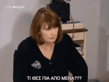 a woman in a black sweater is sitting in a chair and talking to someone in a foreign language .