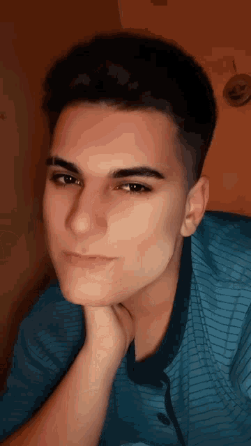 a young man in a blue striped shirt has his hand on his chin