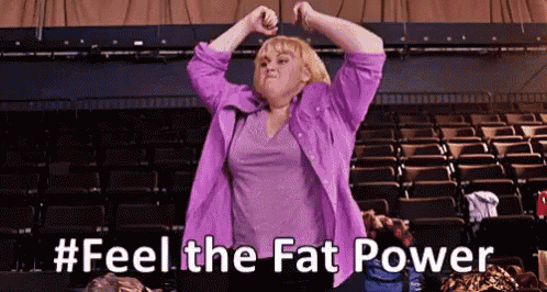 a woman in a purple jacket is standing in an auditorium with her arms in the air and the words `` feel the fat power '' .