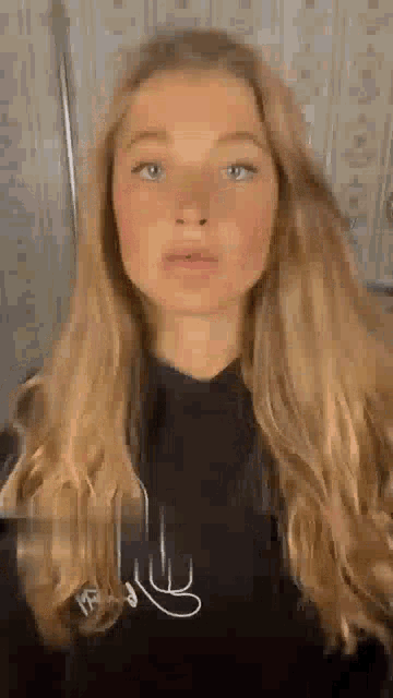 a young woman with long blonde hair and blue eyes is wearing a black hoodie .