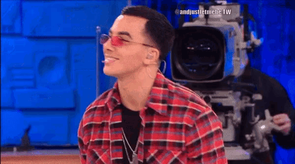 a man wearing sunglasses and a plaid shirt is smiling in front of a camera with the hashtag #andjustthebe tw