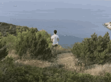 a man in a white shirt is standing on a hill overlooking a body of water