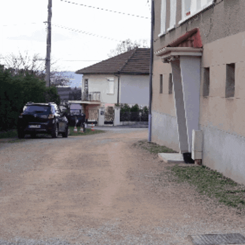 a row of cars are parked on a dirt road in front of a house