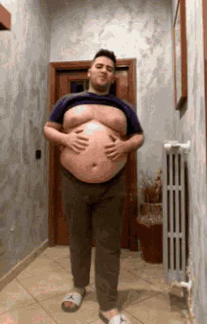 a man with a large belly is standing in a hallway holding his belly
