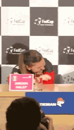 a woman sitting at a table with a pink sign that says simona mulep