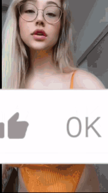 a woman wearing glasses and a yellow bra is holding a sign that says ok