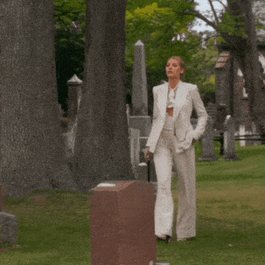 a woman in a white suit walks through a cemetery holding a cane
