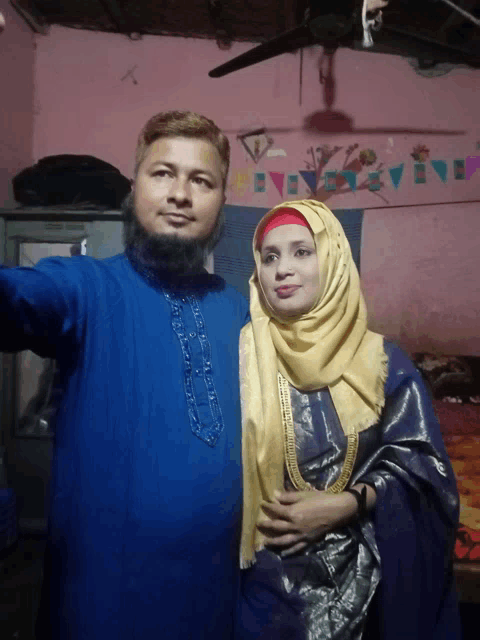a man and a woman pose for a picture in front of a pink wall with flags on it