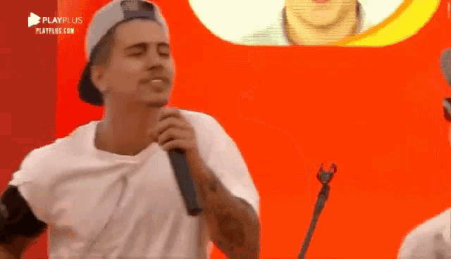 a man singing into a microphone with a playplus logo in the corner