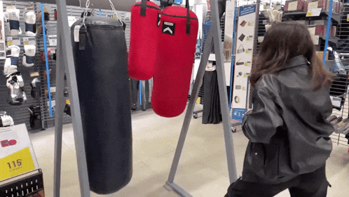 a woman in a leather jacket stands in front of a display of punching bags in a store