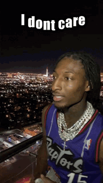 a man wearing a raptors jersey is standing on a balcony overlooking a city at night