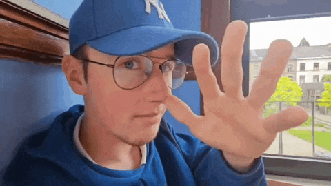 a man wearing a blue hat and glasses is making a stop gesture with his hand .